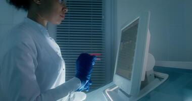 A woman in a lab coat is looking at a computer screen video