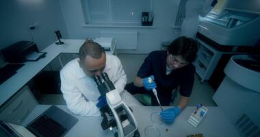 Two people in lab coats working on a microscope video
