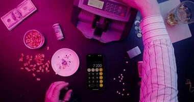 A person using a phone and a calculator next to a pile of money video