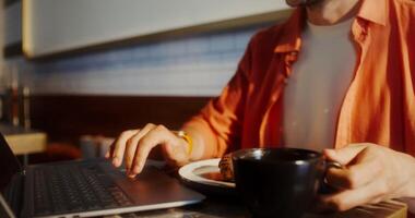 A man is typing on a laptop while holding a coffee video