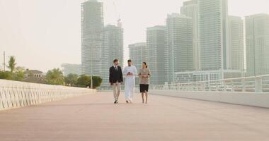 Three people walking on a bridge with tall buildings in the background video