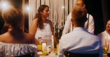 A couple is sitting at a table with candles and a man is standing behind them video