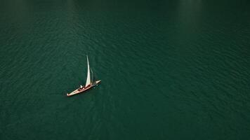 topo Visão do uma barco a vela Navegando dentro a meio do uma lago, girando para dentro uma panorâmico Visão do uma montanha vale com uma ampla lago às a pé do a montanhas, zangão , Suíça video