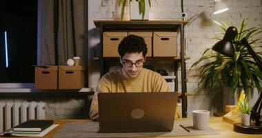 A young dark-haired man achieves success working on a laptop in the office and makes a profit. Dollar bills start to fall from the ceiling, enthralling the man video