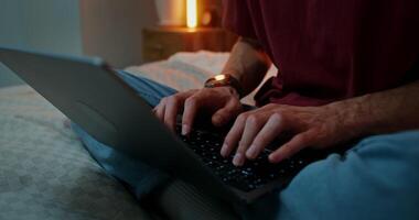 A man is typing on a laptop, standing on his feet, sitting in a lotus position on the bed, Close-up of male hands on the keyboard, no face video