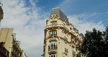 The facade of triangular historical building with a corner at crossroads and widening edges of the walls. Windows and balconies are covered with green vegetation. Paris, France. 4k , red komodo video
