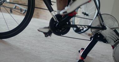 A man in sportswear and shoes for a bicycle trains on a bicycle simulator, practicing standing up riding. Close-up of male legs, dynamic video