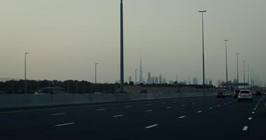 A busy highway on the outskirts of a modern metropolis with glass skyscrapers in the rays of the setting sun video