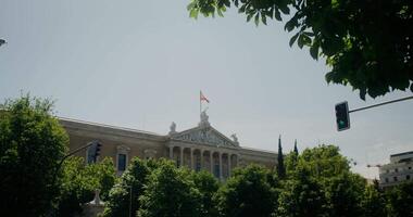 The facade of a historic building with a Spanish flag, visible behind the green crowns of trees video