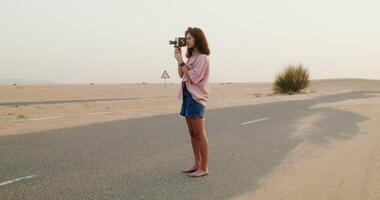 A woman standing in the middle of a desert with a camera video