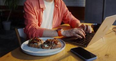 A man sitting at a table with a laptop and food video
