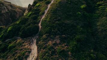 The drone flies over the top of the mountain to the sea with a sandy beach and a rocky reef near the shore. Bird's-eye view on a summer day video