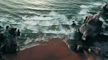 The drone flies over the coastline with a sandy beach between the stone reefs, foam waves hitting the shore video