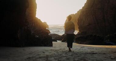 A person walking along the beach in front of a cave video