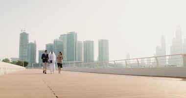 Three people walking on a bridge with tall buildings in the background video