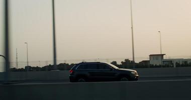 The car is driving along a busy highway, fenced with a grid in the light of the setting sun video