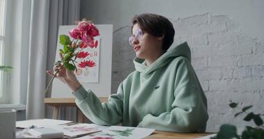 A young female artist admires fresh flowers while looking for inspiration to paint a painting while working in a studio in daylight video