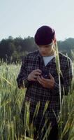 A young man takes photos with a camera, standing between ears of wheat in an agricultural field on a summer sunny day. 4k vertical , red komodo video