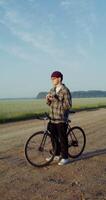A young stylishly dressed man takes photographs with a camera while standing near a picturesque wheat field on a sunny day. 4k vertical , red komodo video