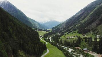 The slopes of the high Alpine mountains, overgrown with a dense spruce forest and the snowy peaks of the rocky mountains, towering above the village, located in the lowland. Drone , Austria video
