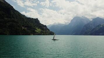 Scenic drone of a sailing boat with a Swiss flag sailing on a beautiful lake at the foot of the Alps, whose peaks are covered with white clouds video