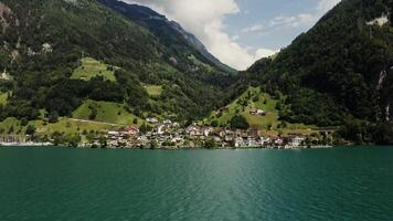 Scenic drone , beautiful view of a modern village with a cottage development in a lowland between the Alpine mountains on the lake shore, from the water side video