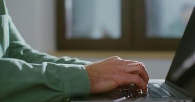 A young man of European appearance is typing on a laptop with a focused look. Gradually shifting the frame from the typing male hands to the serious face of the man video
