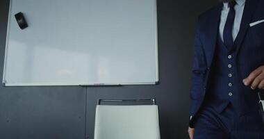 chat, front camera. A man of European appearance with a gray beard, dressed in a business suit starts a chat smiling and waving his hand in sign of greeting, sitting in modern office video