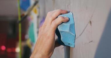 A young man of European appearance climbs up the artificial surface of the climbing wall, grabbing the artificial colored stones on the wall with his hands. Close-up of a hand video