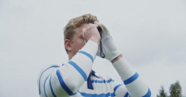 A young handsome man in light-colored clothes and a white golf glove peers through binoculars in search of a hole for a ball, close-up. Golf is a game for the upper class video