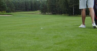 Playing golf on a large, well maintained golf course. Finding a golf ball, picking a golf club and hitting the ball hard. Unidentified person, close-up, shooting in dynamics video