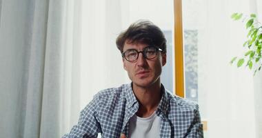 A man in glasses sitting at a table with a laptop video