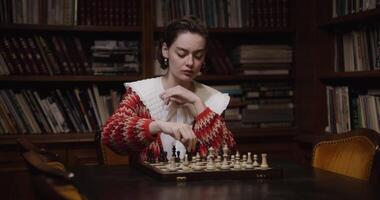 A woman playing chess in front of a bookcase video