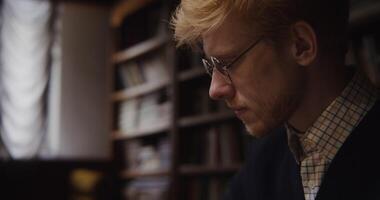 A European-looking man with glasses looks down at the chessboard with concentration, thinking before making a move. Close-up video