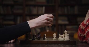 Man and woman playing a chess game sitting opposite each other at a table in the library, close-up of a chessboard video