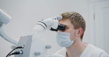 A male dentist of European appearance looks through a dental microscope for the treatment of a patient's tooth root canal. Removal of a nerve in a tooth with a modern method, close-up video