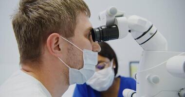 A man in a white shirt and a woman in a mask looking through a microscope video