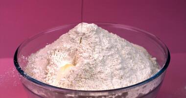 Egg falls into a bowl of flour in slow motion on a pink background video