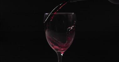 Red wine pouring from bottle into goblet. Close-up of red wine pouring in wine glass at black background. Slow motion. Macro shot with copy space video
