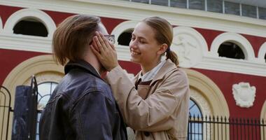 A young beautiful girl sits on the railing and strokes the guy standing next to her on the stairs. Date of a young couple of European appearance on the streets of the city video