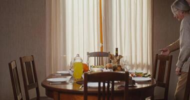 A beautiful family of European appearance from three generations sits down at a festively set table, smiling and talking to each other. Thanksgiving family celebration video