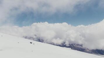 View from a quadcopter to a high-mountainous valley with snow-covered gentle slopes and rocky peaks covered with clouds. Elbrus from a bird's eye view video