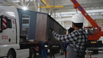 Worker directing modular home loading onto truck via radio video