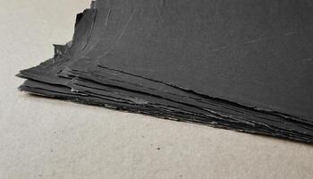 Stack of Textured Black Paper Sheets on Beige Surface in a Studio Lighting photo