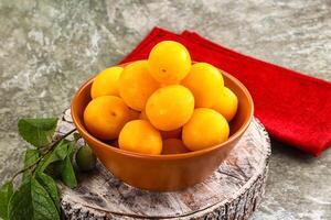 A bowl of yellow plums sitting on a table photo