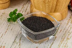 A bowl of black seeds on a table next to a knife photo