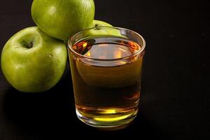 A glass of liquid next to a bunch of green apples photo