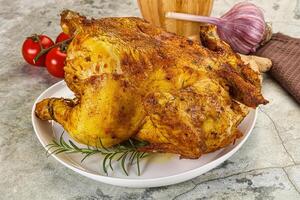 A large roasted chicken on a plate with tomatoes and garlic photo