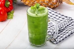 A green drink with a pineapple and pepper on a white table photo