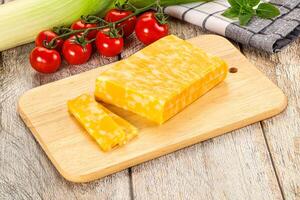 A wooden cutting board with a piece of cheese and vegetables photo